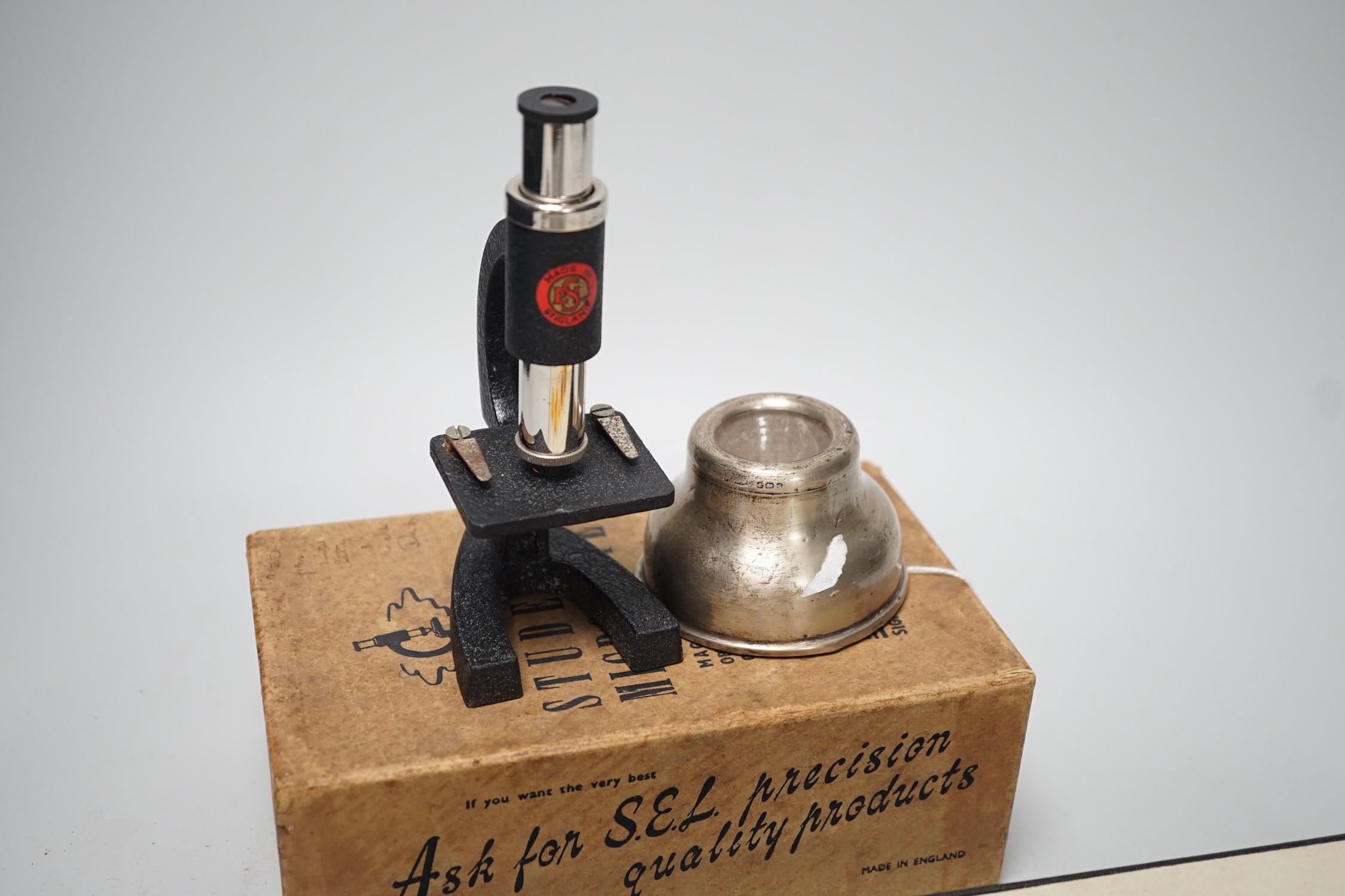 A case of early 20th century microscopes slides and a student's microscope, a small silver inkwell and a small plated figural plaque